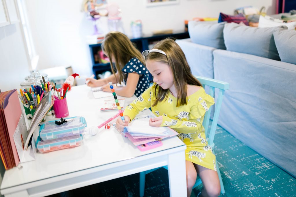 Fashionistas in Training + Nordstrom Kids Clothing by popular Nashville life and style blog, Hello Happiness: image of two girls sitting at a desk and writing in notebooks and wearing a Nordstrom Tea Collection Ruffle Dress, Native Shoes Jefferson Bling Glitter Slip-On Vegan Sneaker, Tucker + Tate Wide Leg Romper, Maniere Metallic Headband, and Mel by Melissa Cosmic Sandal. 