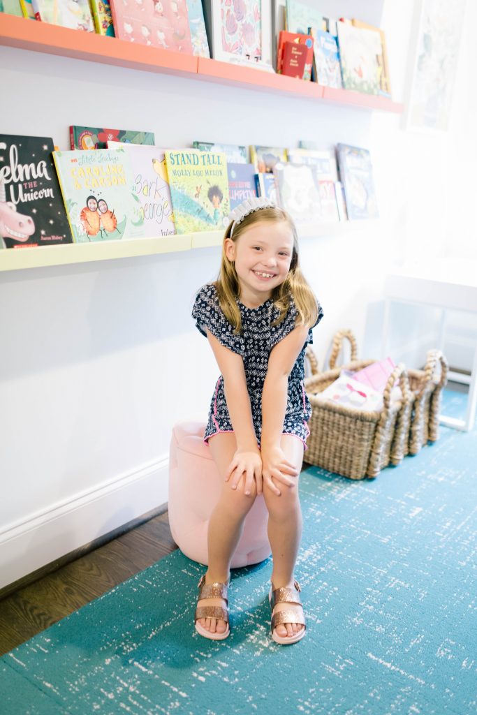 Happy 8th Birthday Daughter by popular Nashville lifestyle blog, Hello Happiness: image of a little girl sitting in front of some floating book shelves. 