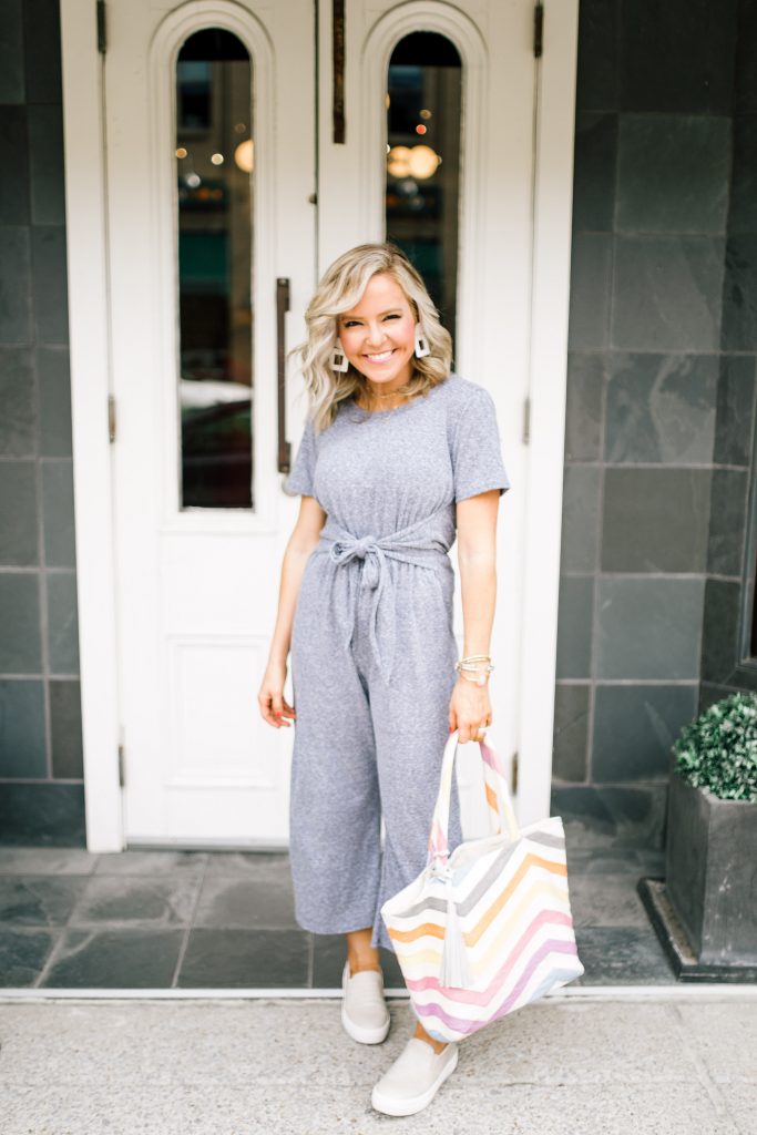 Pretty Pink Lily Favorites...by popular Nashville fashion blog, Hello Happiness: image of a woman wearing a Pink Lily grey Find the Time Jumpsuit, Gills Sneakers, Willa Ford white square earrings, and holding a Striped Jaunt Tote.  