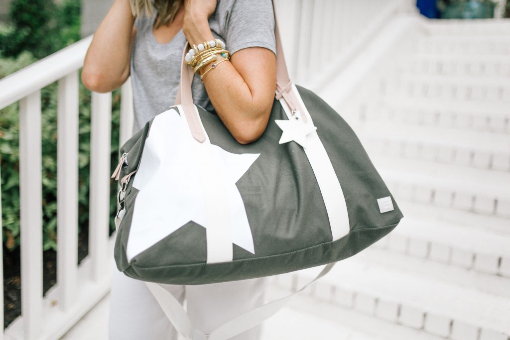 We Dress America + Walmart Travel Style for a Successful Getaway by top US fashion blog, Hello Happiness: image of woman holding large gray duffle bag with white star print and white straps.