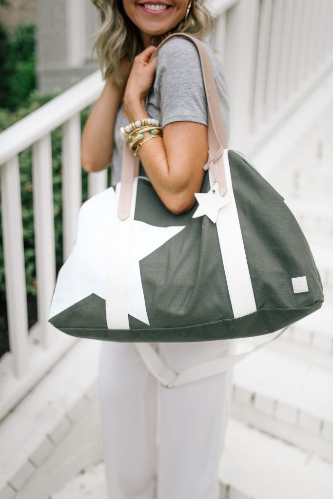 We Dress America + Walmart Travel Style for a Successful Getaway by top US fashion blog, Hello Happiness: image of a smiling woman holding large gray duffle bag with white star print and white straps.