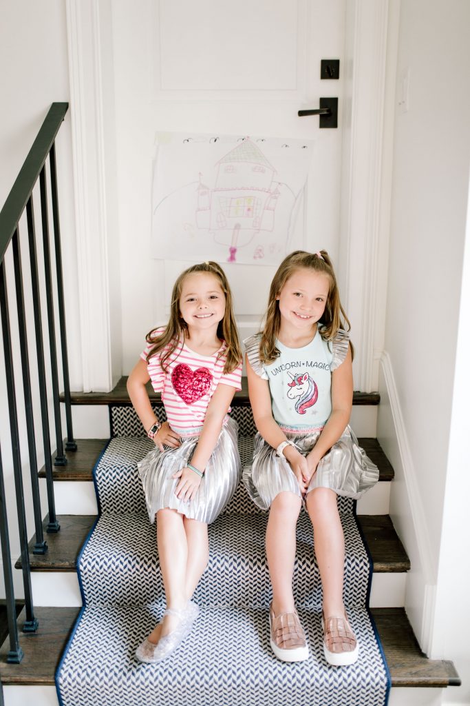 Trend Setting Back-to-School Outfits from Walmart by popular Nashville fashion blog, Hello Happiness: image of two girls sitting on some stairs and wearing Walmart 365 Kids From Garanimals Shimmer Foil Pleated Skirt and 365 Kids From Garanimals Flutter Graphic Tank Top. 