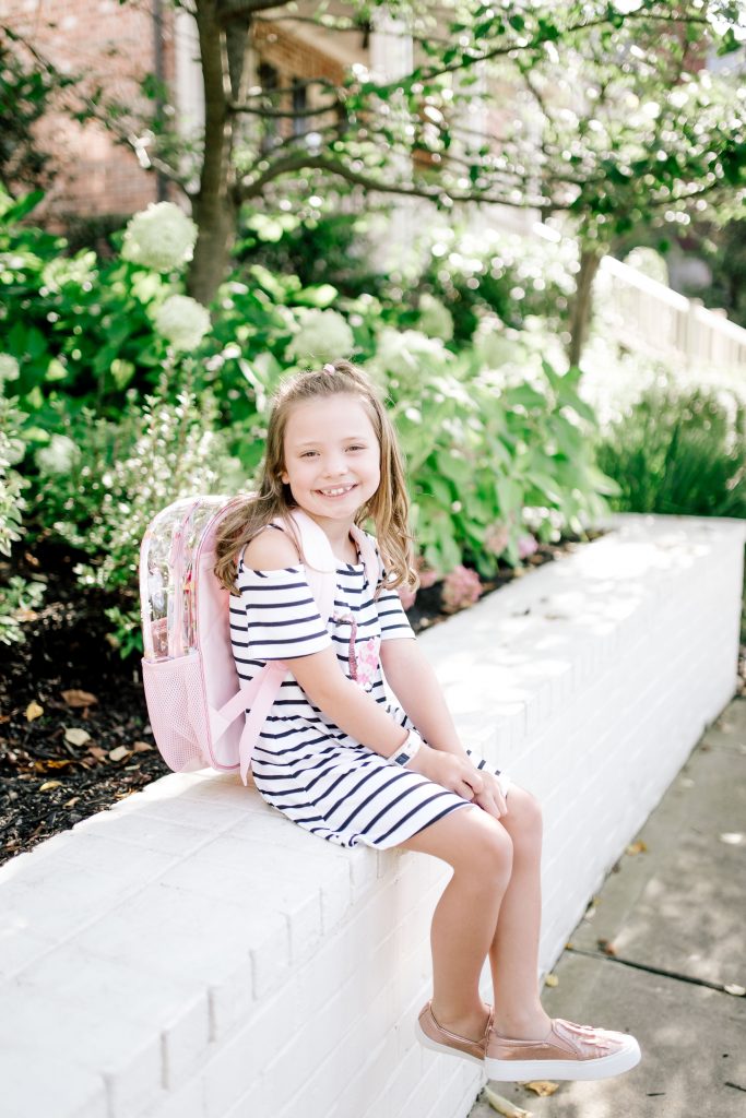 Walmart Back to School Style for 2nd Grade! by popular Nashville fashion blog, Hello Happiness: image of a girl sitting outside and wearing a Walmart Sequin Flamingo Bow Back Dress, Wonder Nation Girls' Casual Ruffle Slip On Sneaker, and Wonder Nation Clear Kids Backpack.
