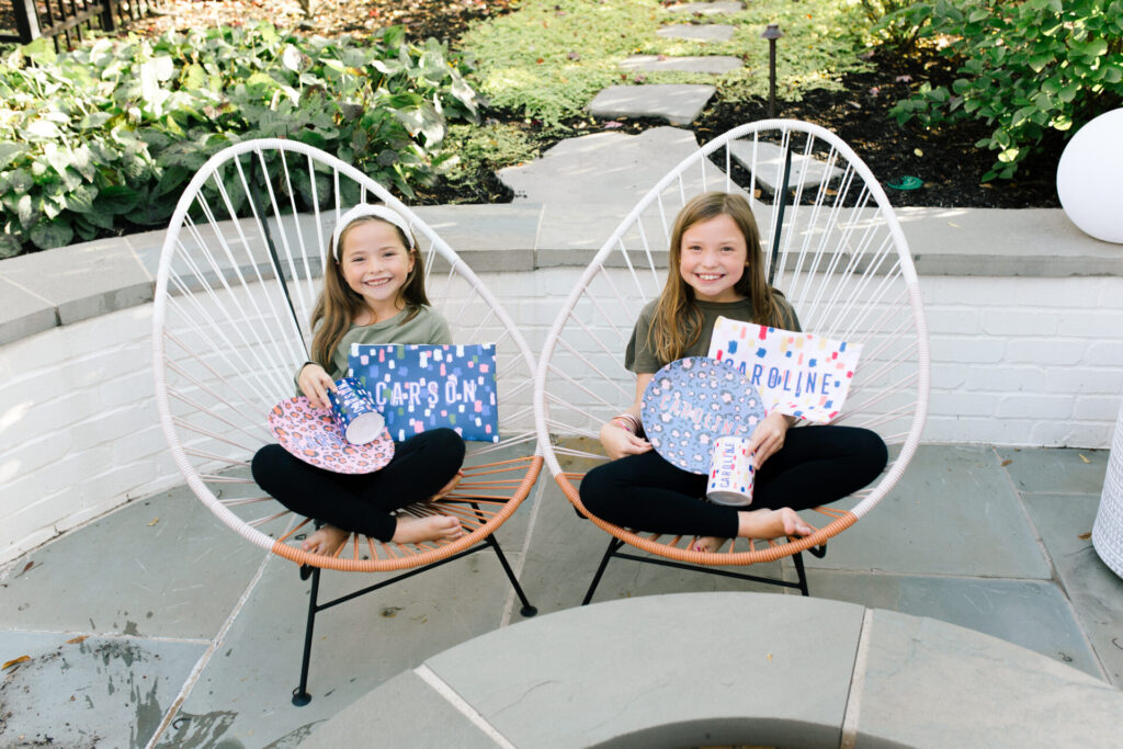 Clairebella Studio by popular Nashville life and style blog, Hello Happiness: image of two young girls sitting outside and holding Clairebella Studio and Hello Happiness personalized tumblers, dinner plates, and zippered bags. 