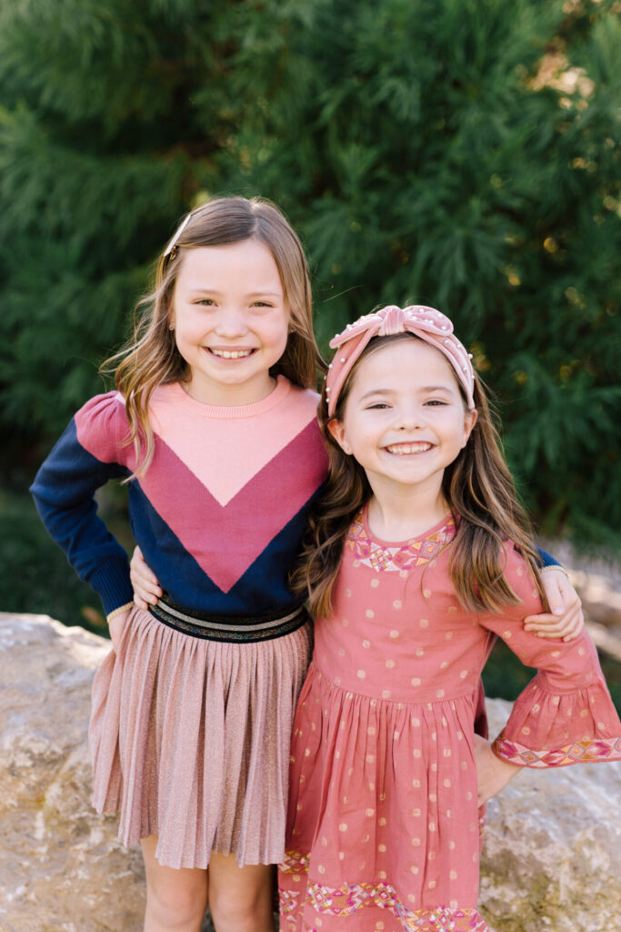 Year in Review by popular Nashville lifestyle blog, Hello Happiness: image of two young girls standing together outside and wearing a pink dress, pleated pink skirt, puff sleeve sweater, and knot headband. 