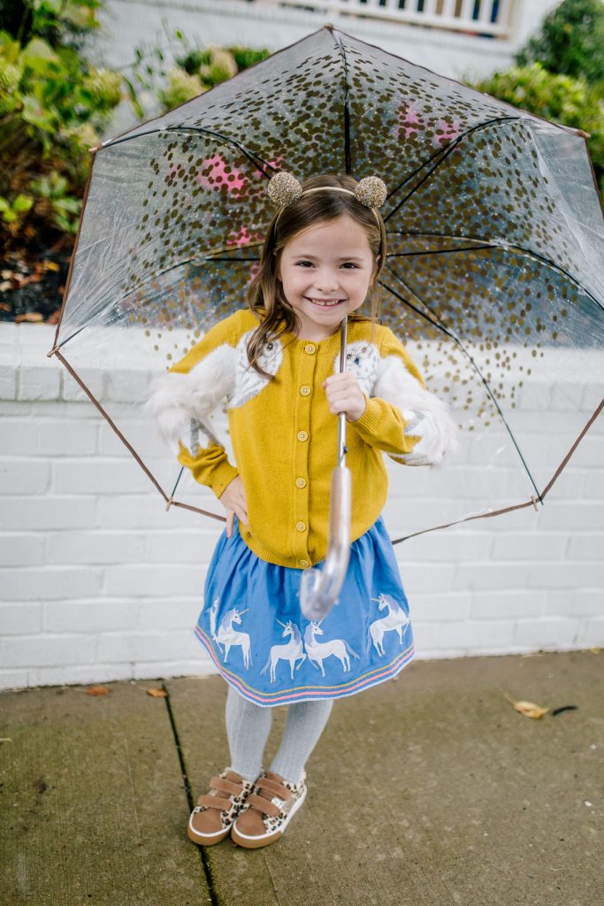 Party-Worthy Looks with the Boden Harry Potter Collection by popular Nashville fashion blog, Hello Happiness: image of a girl standing outside with an umbrella and wearing a Boden Hedwig Cardigan, Boden Appliqué Hem Skirt, Boden Grey Marl Ribbed Tights, and Boden Fun Low Tops.