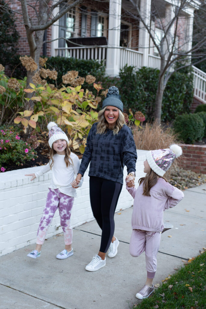 Nordstrom Fashion by popular Nashville fashion blog, Hello Happiness: image of Natasha Stoneking walking outside with her two girls and wearing a Tucker and Tate sequin pom beanie, Nordstrom Zella Girl Kids' Cozy Active Pullover, Nordstrom Zella Girl Kids' Velour Cozy Active Joggers, Zella Girl Kids' Tie Dye Joggers, Zella Girl Kids' Peaceful Twist Front T-Shirt, Zella pom beanie, Zella 7/8 leggings, and Zella Carey Crew Hi/Low Sweatshirt.