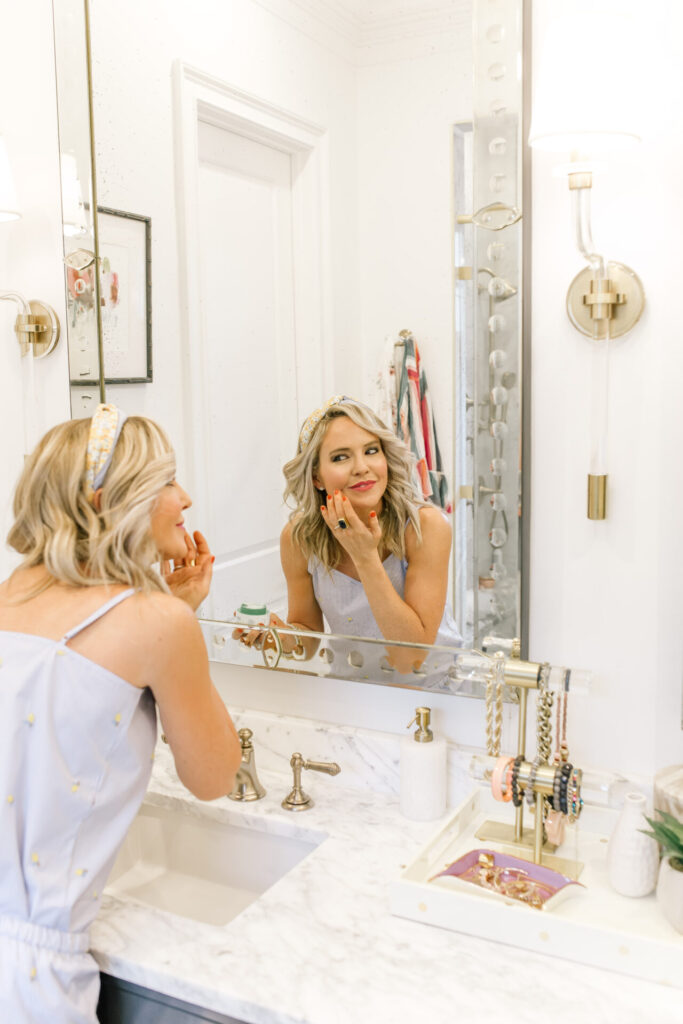 Sephora Spring Sale by popular Nashville beauty blog, Hello Happiness: image of a woman looking at herself in her bathroom mirror as she applies makeup.