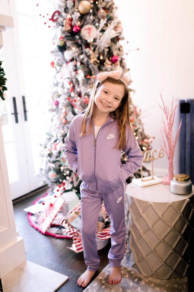 Happy 8th Birthday Daughter by popular Nashville lifestyle blog, Hello Happiness: image of a little girl wearing a Nike track suit and standing in front of a Christmas tree. 