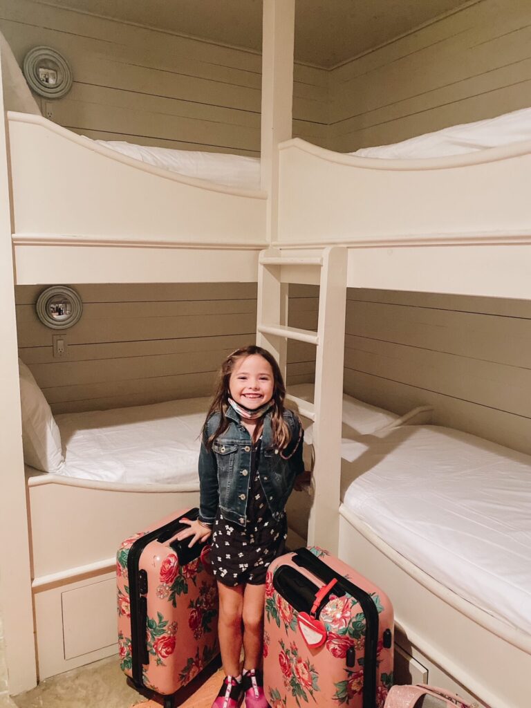 Rosemary Beach by popular Nashville travel blog, Hello Happiness: image of a young girl standing next to two floral print suitcases in a bunk room. 