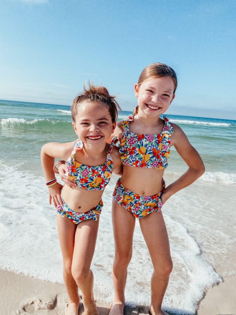 Rosemary Beach by popular Nashville travel blog, Hello Happiness: image of two girls standing together in ocean surf and wearing matching swimsuits. 