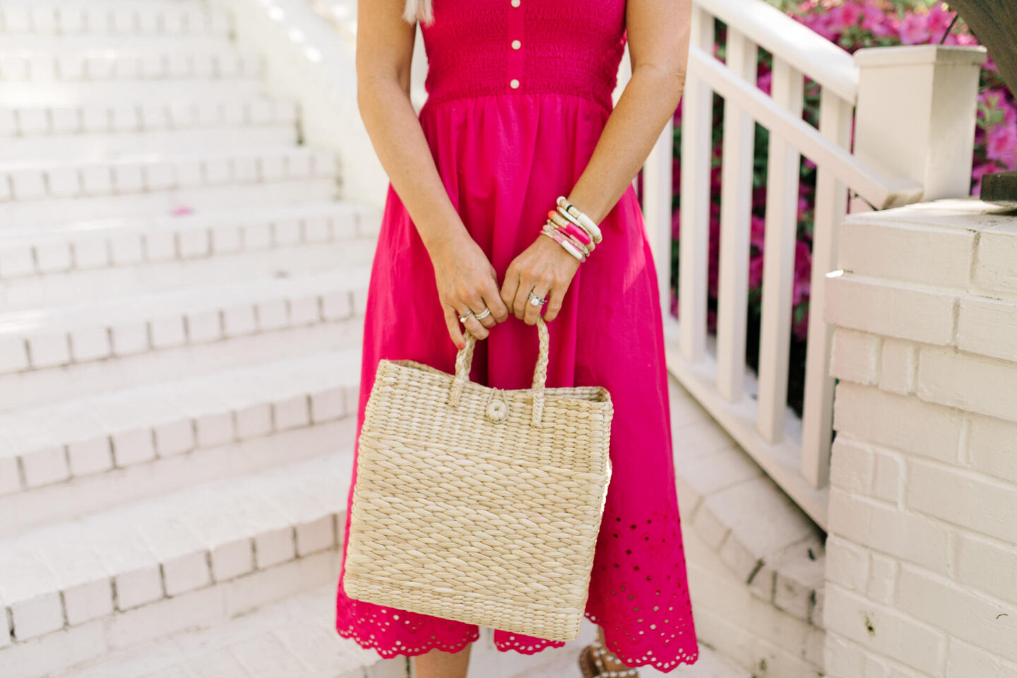 Summer Dress by popular Nashville fashion blog, Hello Happiness: image of a woman standing on some white brick stairs and wearing a pink eyes hem midi dress travel pearl sandals, and holding a woven tote. 