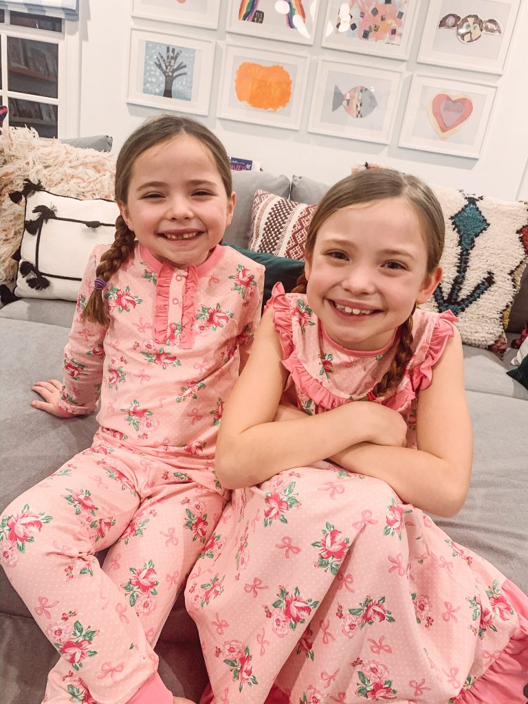 All About the Love... What to Wear on Valentine's Day by popular Nashville fashion blog, Hello Happiness: image of two little girls sitting together and wearing Smocked Auctions BEAUTIFUL DREAMS GIRLS HENLEY LOUNGEWEAR PINK and Smocked Auctions BEAUTIFUL DREAMS GOWN PINK KNIT.