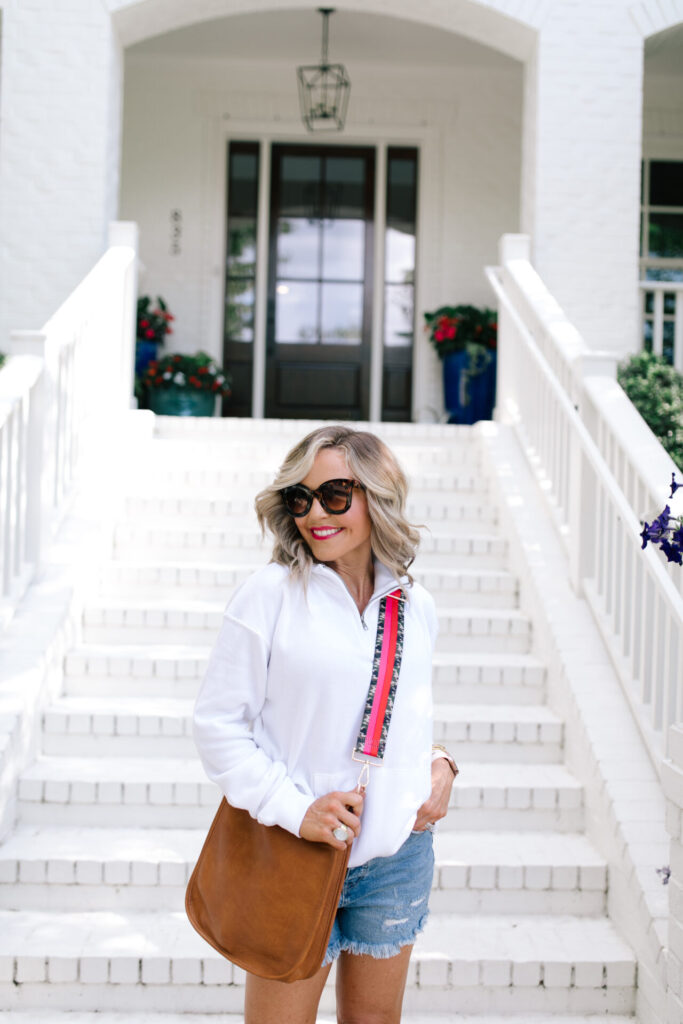 Labor Day Sales by popular Nashville fashion blog, Hello Happiness: image of a Natasha Stoneking wearing a pair of Free People CRVY High Rise Cut Offs, white half zip pullover sweatshirt, and carrying a Vegan Messenger Bag with a Blogger Collaboration Bag Strap. 