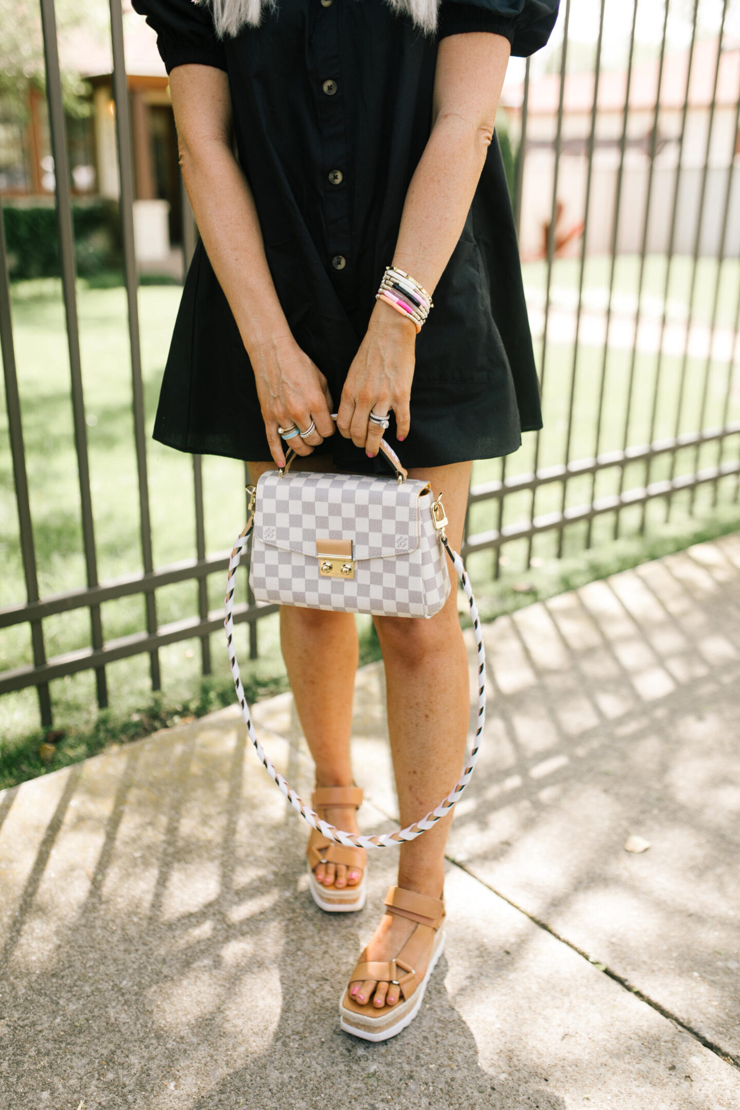 Rompers and Jumpers by popular Nashville fashion blog, Hello Happiness: image of a woman standing in front of a wrought iron fence and wearing a black off the shoulder romper, sunglasses, and holding a grey and white checker handbag. 