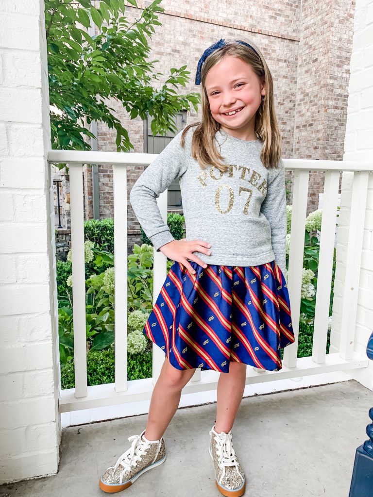 The Magical World of the Mini Boden Harry Potter Collection by popular Nashville fashion blog, Hello Happiness: image of a girl standing outside and wearing Mini Boden Sequin Seeker Dress, Mini Boden High Tops, and a blue sequin bow headband.