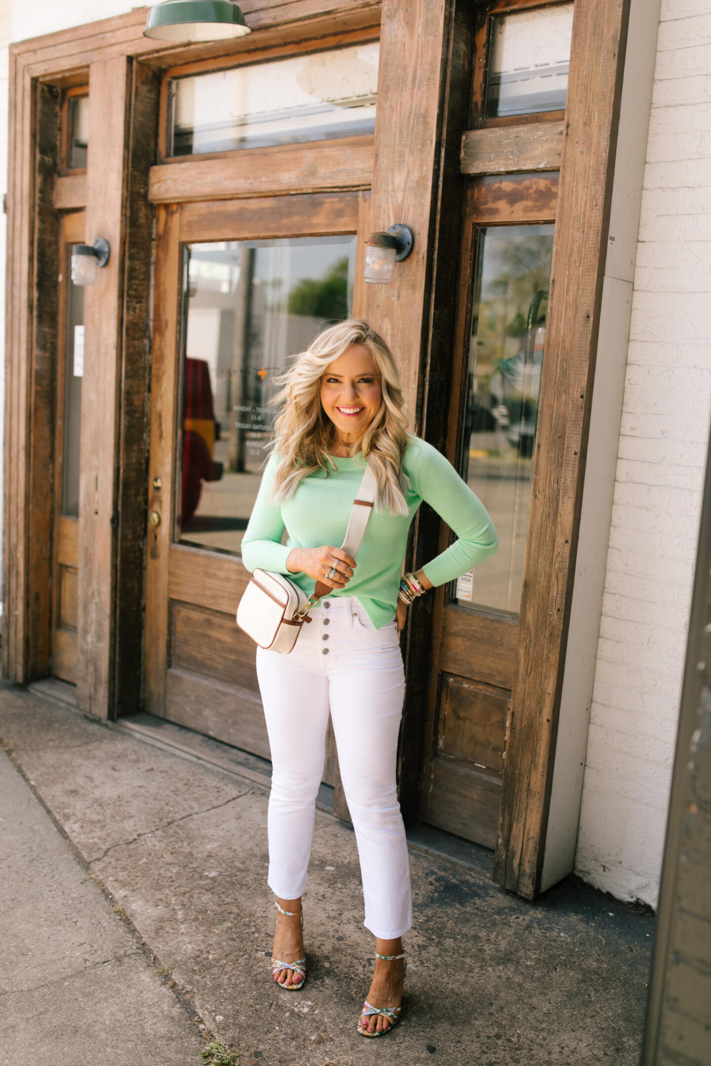 J Crew Clothing by popular Nashville fashion blog, Hello Happiness: image of a woman wearing a J Crew green long sleeve shirt and 10" demi boot crop jean in white with a pair of floral print strap sandals. 