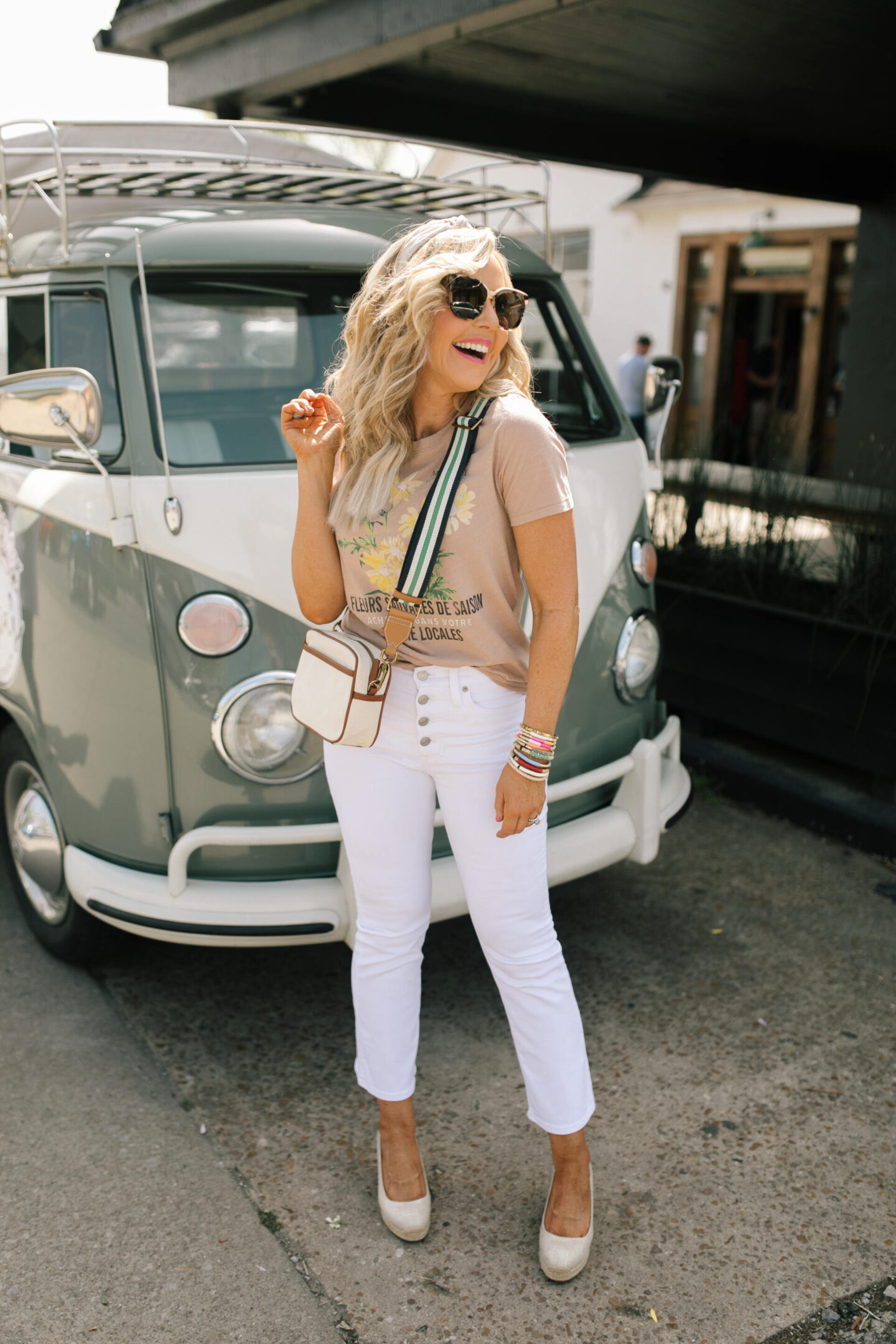 Memorial Day Sales by popular Nashville life and style blog, Hello Happiness: image of Natasha Stoneking standing in front of a VW van and wearing a J Crew floral graphic tee, white Demi crop denim, gold espadrilles, and camera bag with a Social Threads stripe strap. 