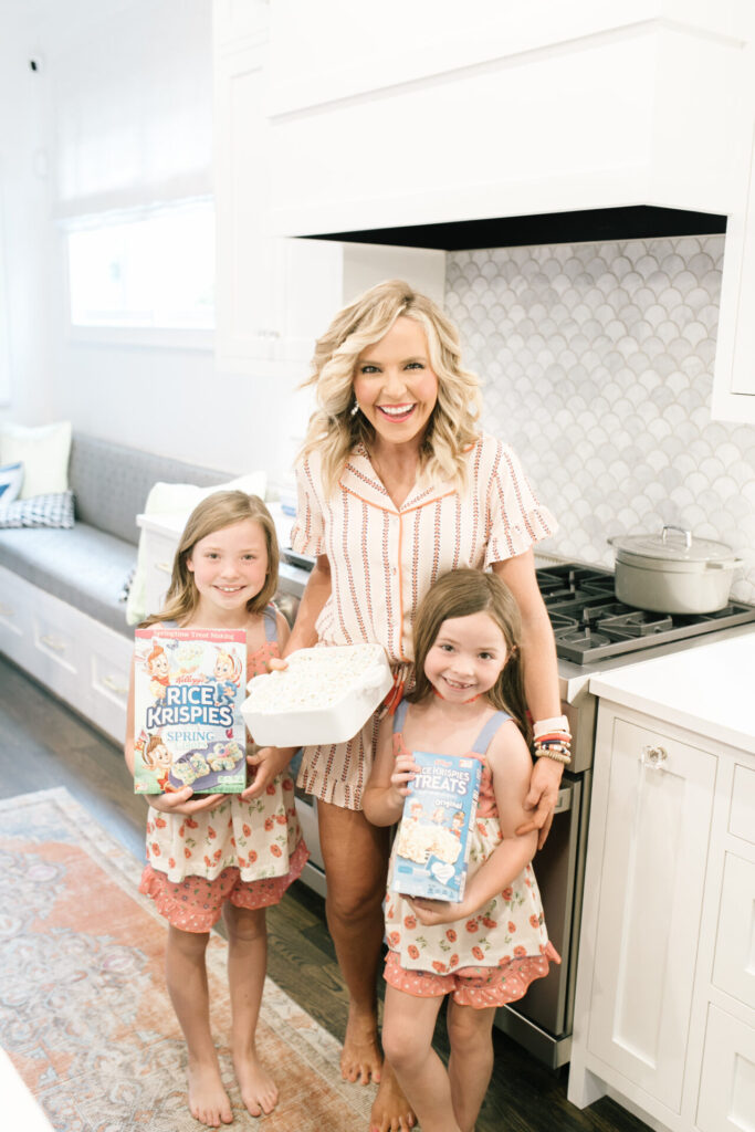 What COVID-19 Has Taught Me by popular Nashville lifestyle blog, Hello Happiness: image of a woman standing in her kitchen with her two daughters while they hold Rice Krispies boxes and a tray of Rice Krispies treats while wearing a fast asleep PJ set and perfect night PJ set.  