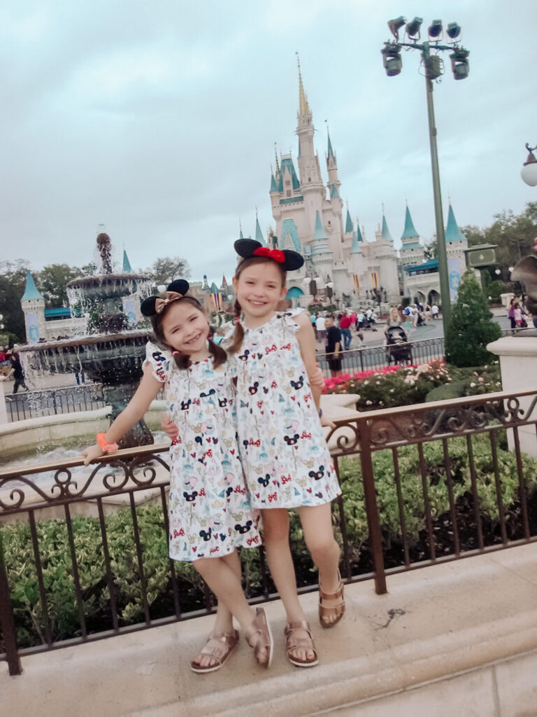 Disney Creators Celebration by popular Nashville lifestyle blog, Hello Happiness: image of two girls standing in front of the Disneyland castle and wearing a PREORDER MAGIC FLUTTER DRESS, Zappos rose gold Birkenstocks sandals, and Disney Minnie ears. 