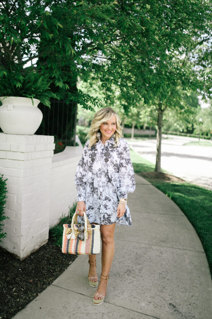 Anthropologie Sale by popular Nashville fashion blog, Hello Happiness: image of a woman standing outside and wearing a Anthropologie Lavinia Embroidered Shirtdress, See by Chloe Glyn Wedge Espadrilles, Hearne Dry Goods Co.Flower Dangle White, and holding a VINCE CAMUTO EMEI SMALL TOTE. 
