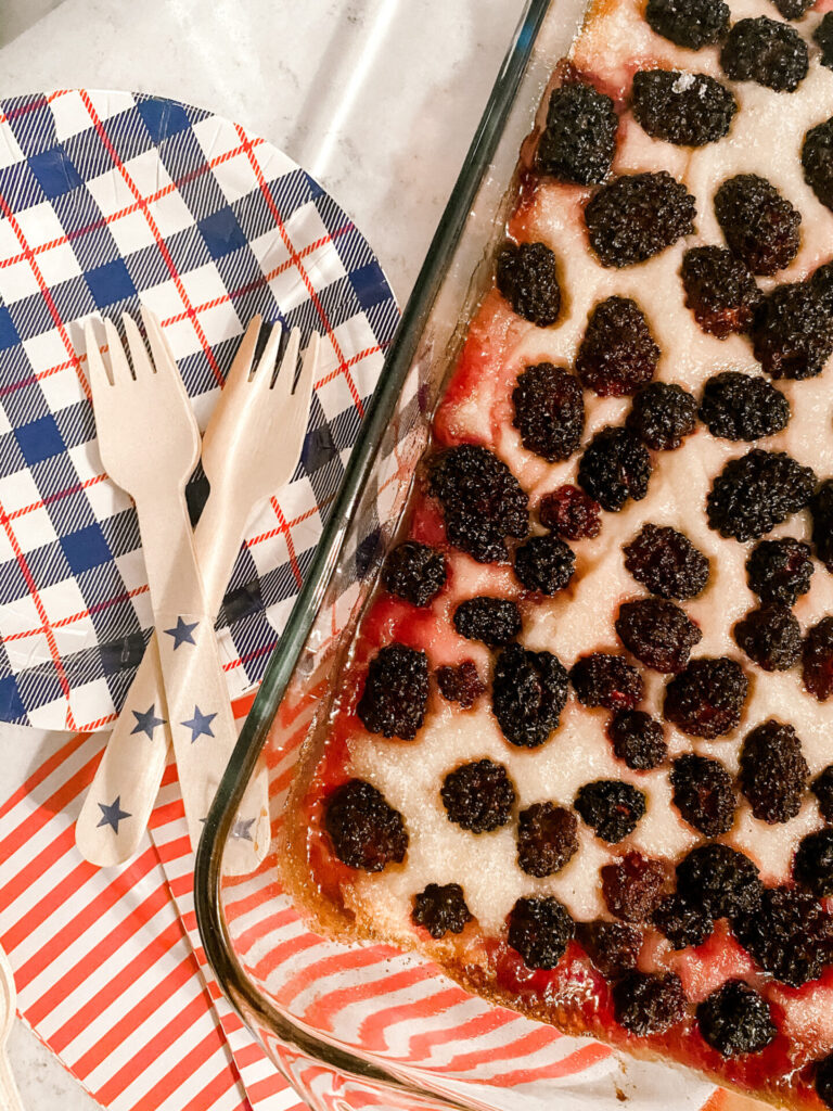 Blackberry Cobbler by popular Nashville lifestyle blog, Hello Happiness: image of wooden forks, red, white, and blue paper plates, and blackberry cobbler in a pyrex baking dish. 