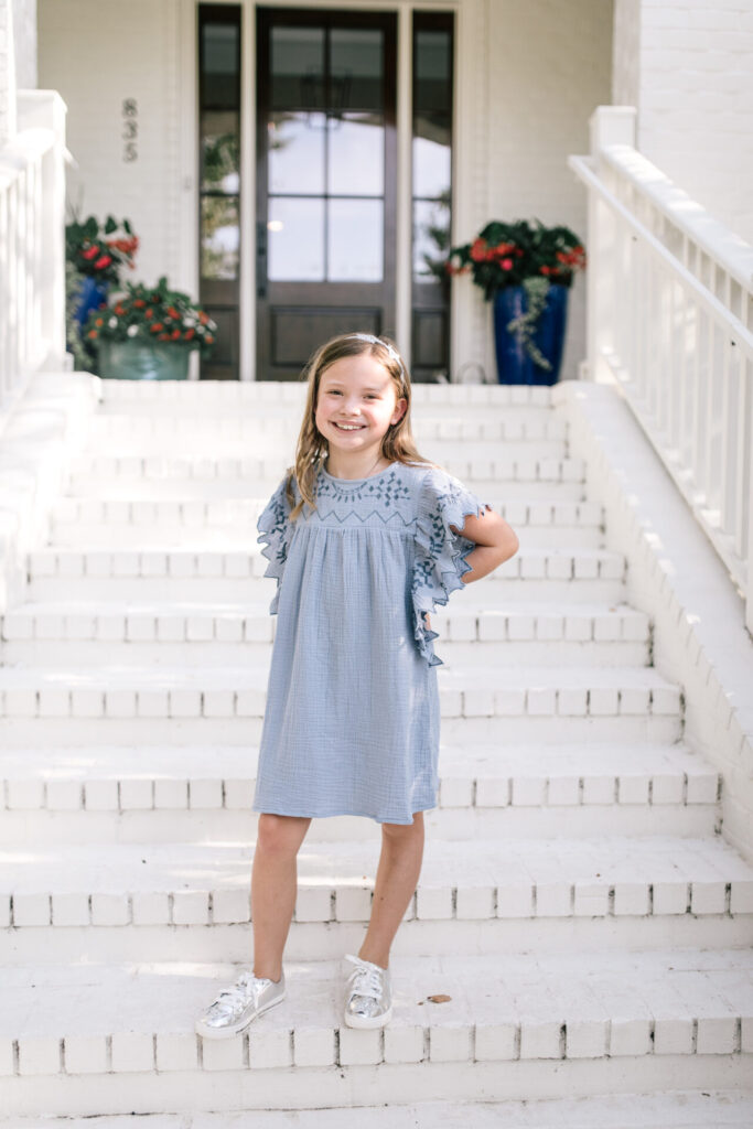 Walmart School Clothes by popular Nashville fashion blog, Hello Happiness: image of a young girl standing on her front porch steps and wearing a Walmart Cotton On Kids Girls Maggie Flutter Sleeve Dress.