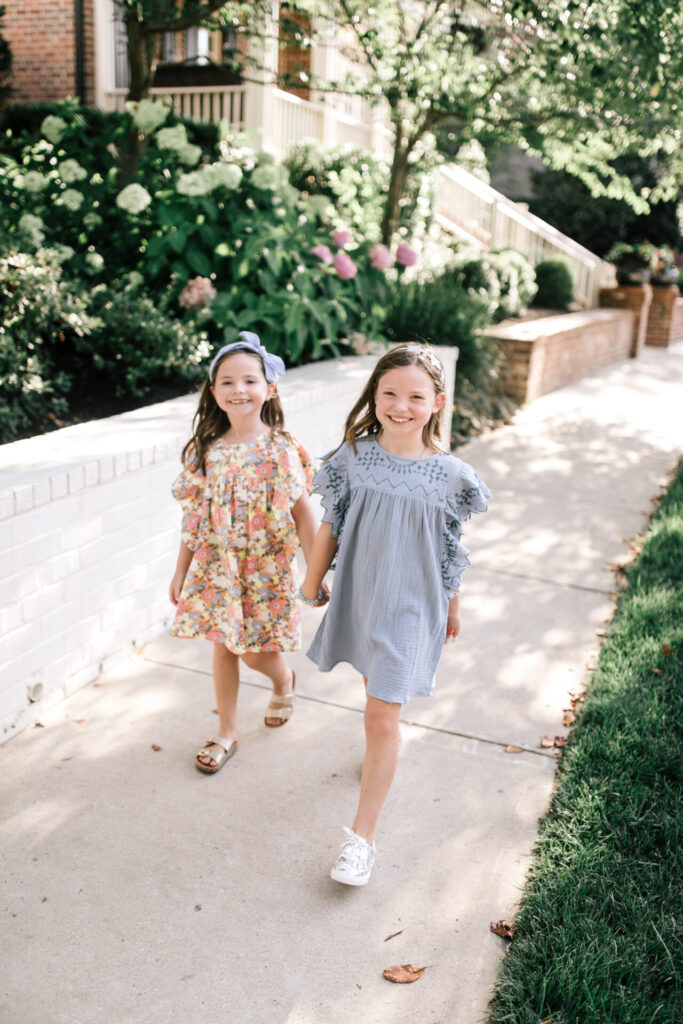 Walmart School Clothes by popular Nashville fashion blog, Hello Happiness: image of two sisters walking together outside and wearing Walmart Cotton On Kids Girls Maggie Flutter Sleeve Dresses.