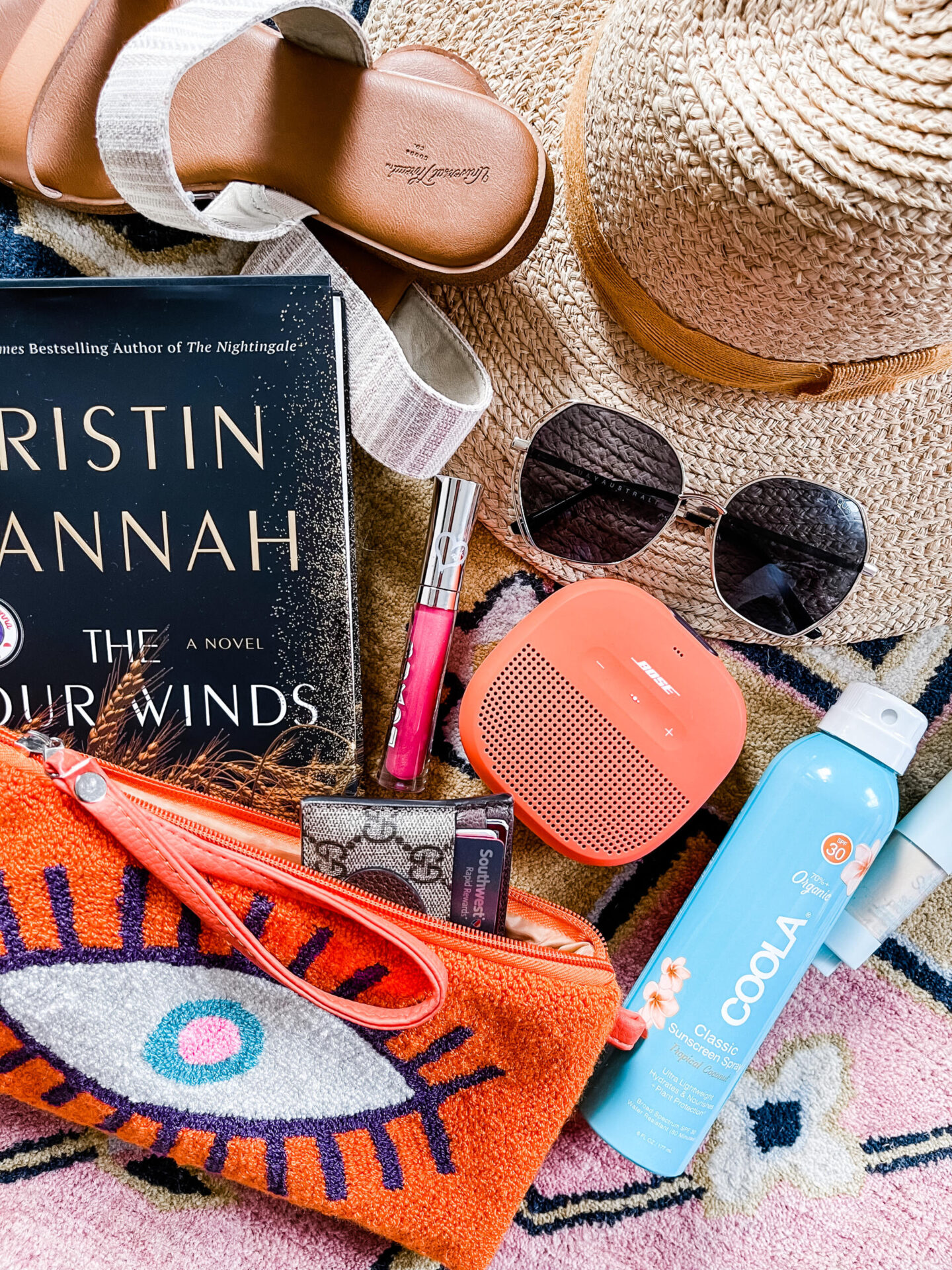 Anthropologie Sale by popular Nashville life and style blog, Hello Happiness: image of an evil eye clutch, straw sunhat, sunglasses, coola spray sunscreen, The Four Winds book, Boxom lipgloss, and a Bose bluetooth speaker. 