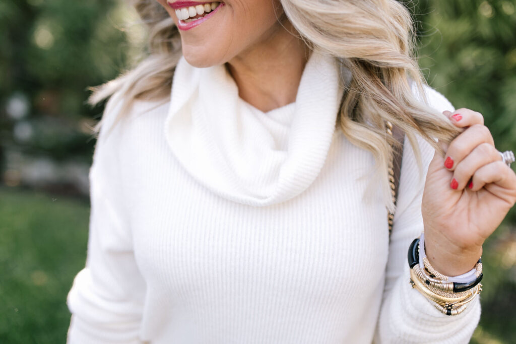 Gibsonlook by popular Nashville fashion blog, Hello Happiness: image of a woman wearing a white slouch neck sweater and black and gold stack bracelets. 