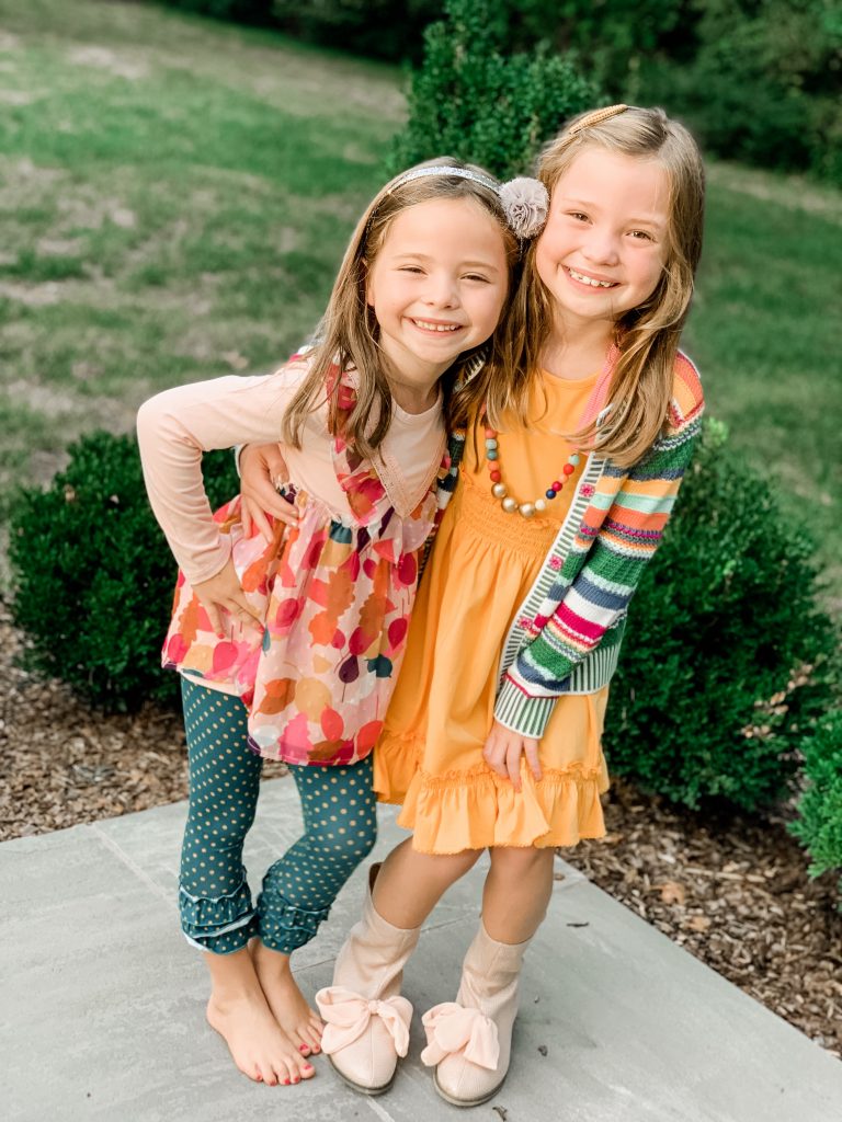 Caroline and Carson's Daily Style... Fall Fashion 2019 Edition by popular Nashville fashion blog, Hello Happiness: image of two little girls standing next to each other outside and wearing a Matilda Jane Clothing Long-Sleeved Lap Dress, Matilda Jane Clothing Leaf Pile Tunic, Matilda Jane Clothing Community Garden Legging, and Matilda Jane Clothing Hip And Hygge Cardigan.