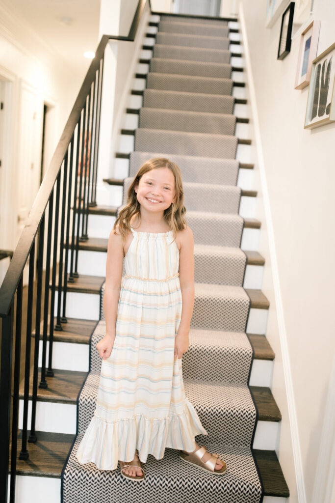 Walmart Back to School by popular Nashville life and style blog, Hello Happiness: image of a young girl standing on a stair case and wearing a Walmart Jessica Simpson Girls Halter Neck Striped Maxi Dress, and Walmart bebe Girls Big Kid Two Buckle Strap Cork Footbed Slide Sandals Rose Gold.