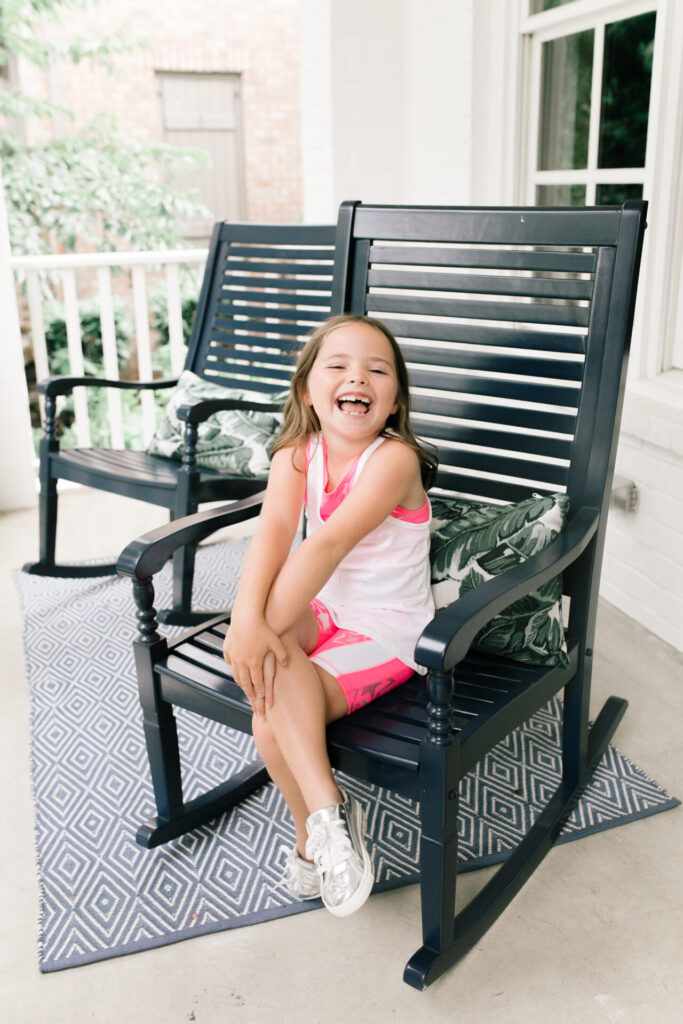 Walmart Back to School by popular Nashville life and style blog, Hello Happiness: image of a young girl sitting outside in a black rocking chair and wearing a Walmart Athletic Works Girls Active 2-Fer Tank and Bike Printed Bike Shorts.
