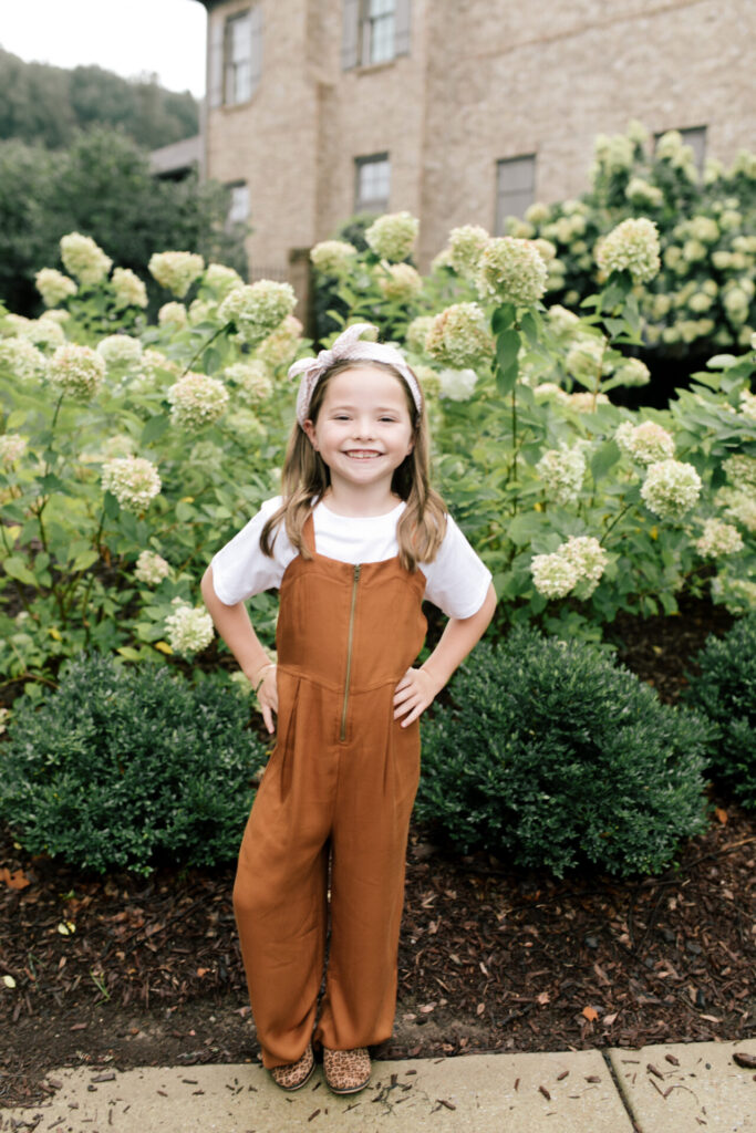 Tween Fashion by popular Nashville fashion blog, Hello Happiness: image of a girl sanding outside in front of a bush with white flowers and wearing a Target zip front utility jumpsuit, Target classic boxy t-shirt, and Target leopard print booties. 