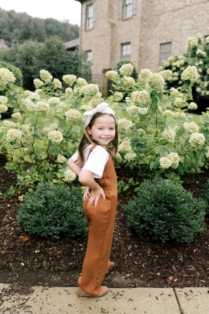 Tween Fashion by popular Nashville fashion blog, Hello Happiness: image of a girl sanding outside in front of a bush with white flowers and wearing a Target zip front utility jumpsuit, Target classic boxy t-shirt, and Target leopard print booties. 