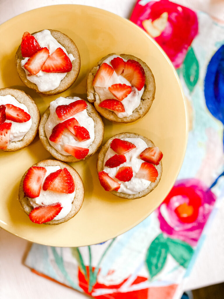 Strawberry Shortcake Cookie Cups by popular Nashville lifestyle blog, Hello Happiness: image of some strawberry shortcake cookie cups on a yellow cake stand. 