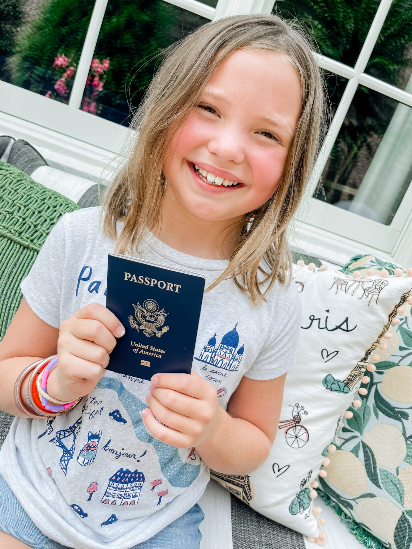 Traveling With Kids by popular Nashville travel blog, Hello Happiness: image of a young girl wearing a Paris graphic image t-shirt and holding a passport in her hands. 