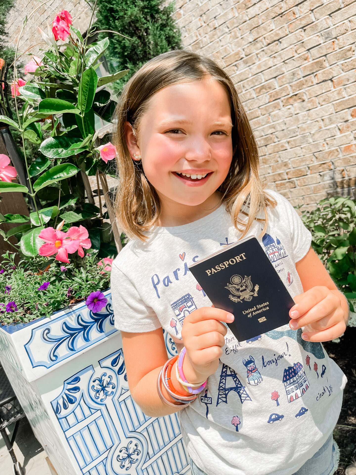 Traveling With Kids by popular Nashville travel blog, Hello Happiness: image of a young girl wearing a Paris graphic t-shirt and holding a passport in her hands. 