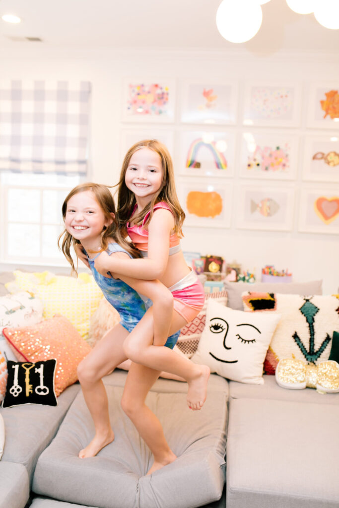 Tween Fashion by popular Nashville fashion blog, Hello Happiness: image of two girls wearing a Target sports bra, Target gym shorts, Target blue galaxy leotard, and Target gym shorts and standing on a grey couch while one girl gives the other girl a piggy back.