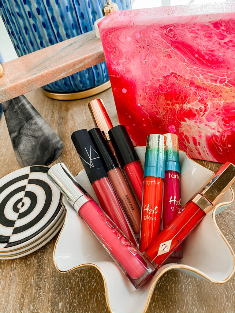 Spring Lip Glosses by popular Nashville beauty blog, Hello Happiness: image of a white ceramic trinket dish filled with various red and pink lip glosses.