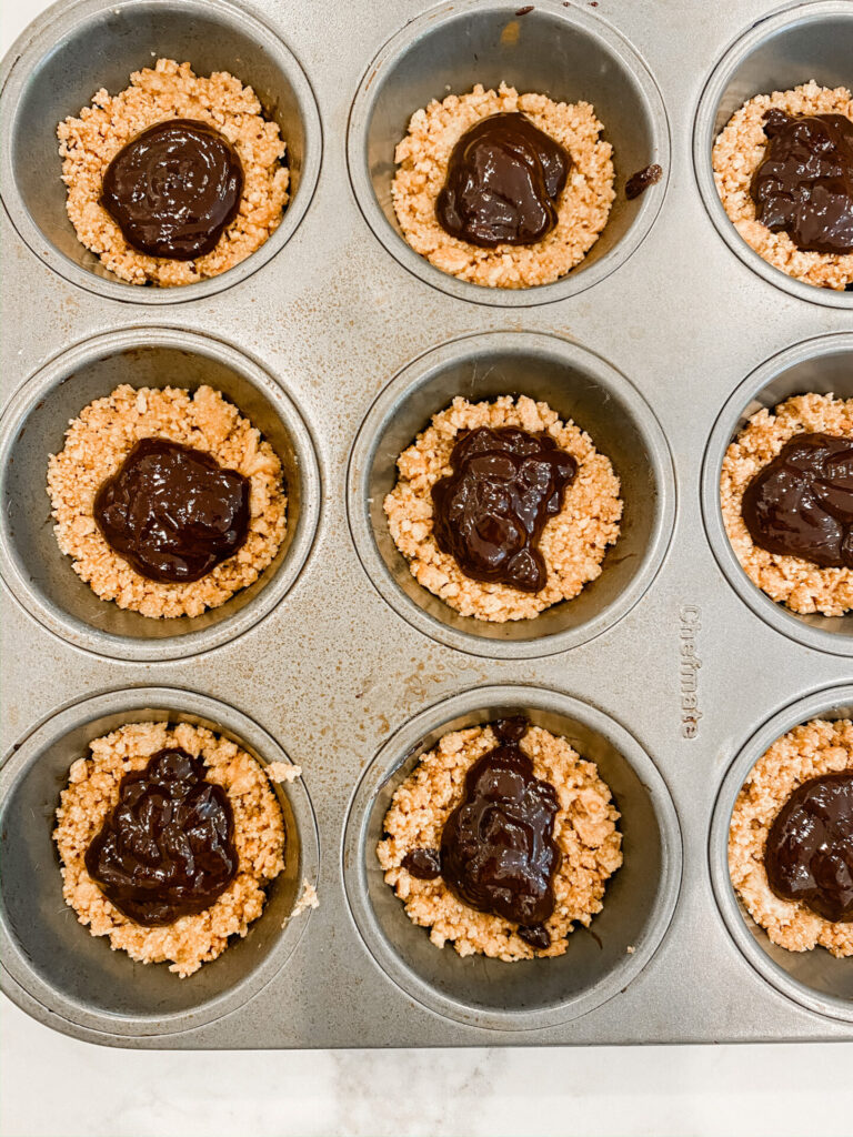 Frozen S'mores Cups by popular Nashville lifestyle blog, Hello Happiness: image of the graham cracker crusts topped with chocolate in muffin tins. 
