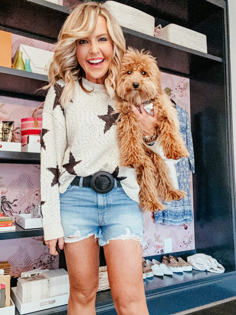 Puppy Products by popular Nashville life and style blog, Hello Happiness: image of a woman holding her 6 month old teacup golden doodle dog and wearing a Vici MAKE HEADLINES KNIT STAR SWEATER, Vici HAZEL HIGH RISE DISTRESSED DENIM SHORTS, and Vici MARCELLA STRAW BELT.