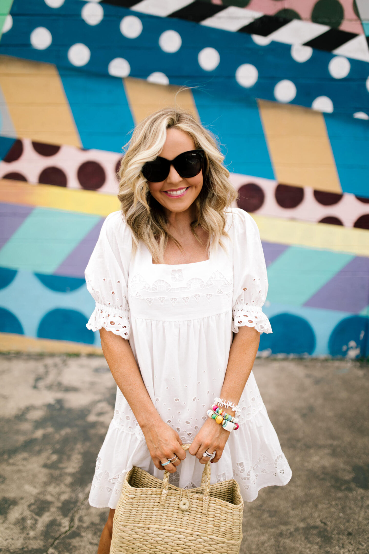 Collaborations and Partnerships by popular Nashville lifestyle blog, Hello Happiness: image of a woman standing in front of a abstract wall mural and wearing a white eyelet dress and holding a seagrass tote. 