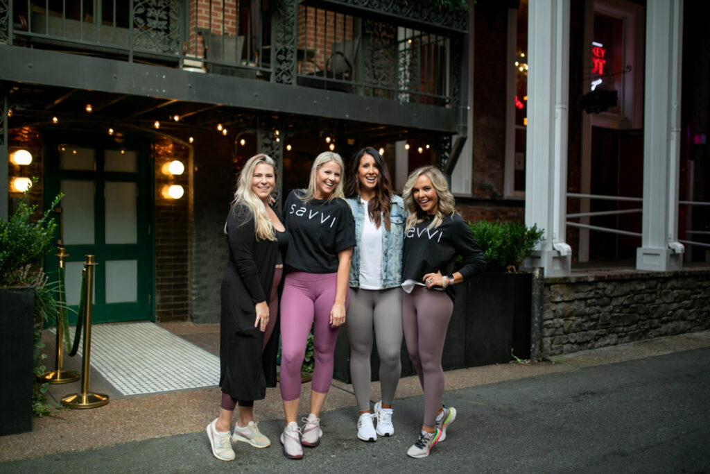 Savvi by popular Nashville fashion blog, Hello Happiness: image of four women standing together outside of a building and wearing Savvi leggings, Savvi t-shirts, and athletic sneakers.  