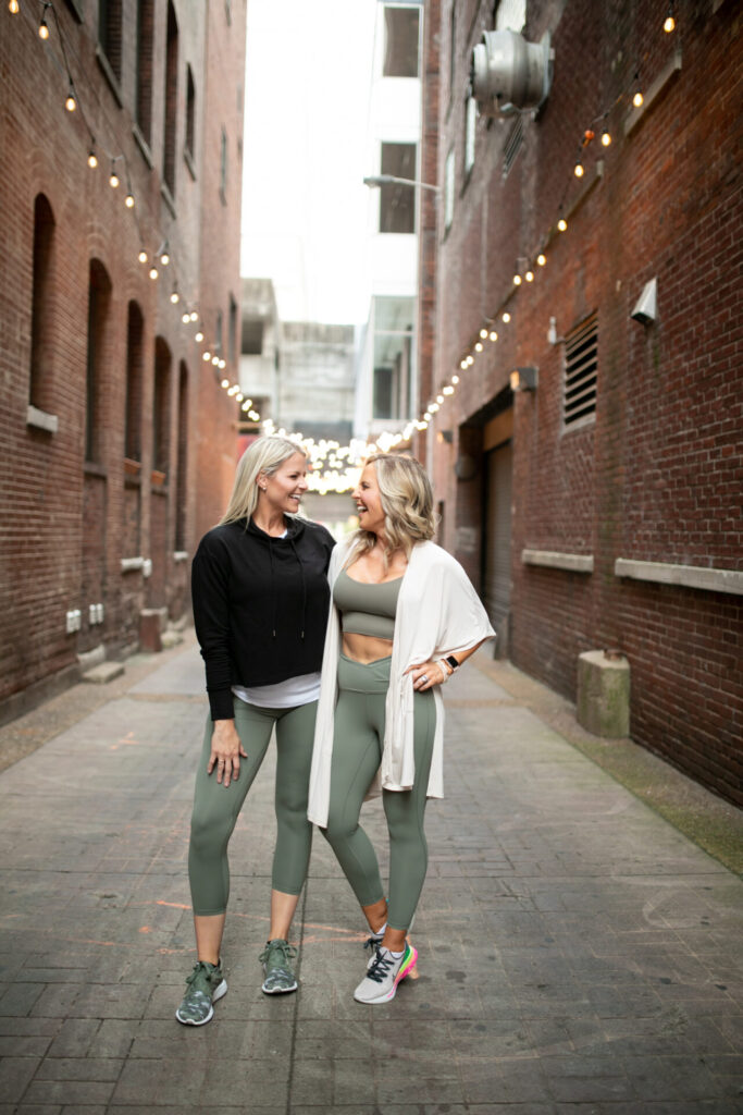 Faster Way to Fat Loss by popular Nashville lifestyle blog, Hello Happiness: image of two women wearing athleticwear and standing together in an alley way. 