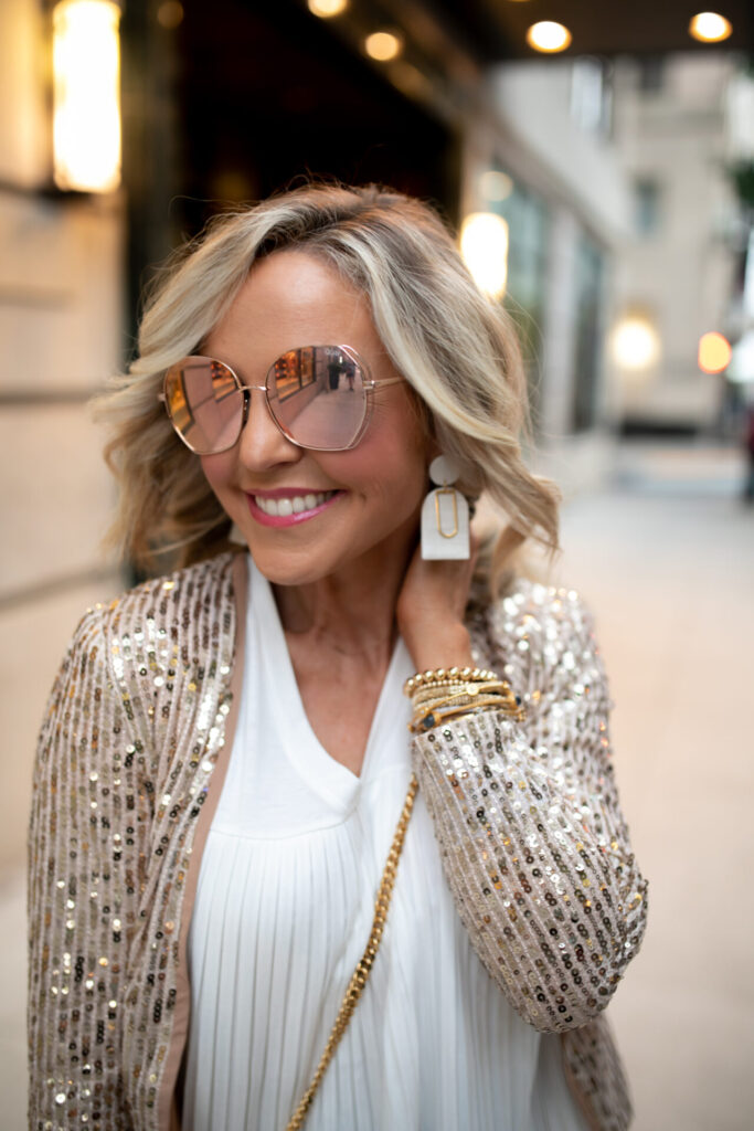 Fake Tan by popular Nashville beauty blog, Hello Happiness: image of a woman in downtown Nashville wearing a Molly Bracken SEQUINED BLAZER, Molly Bracken pleated top, MLDED Clay earrings, and Quay Australia Big Love sunglasses. 