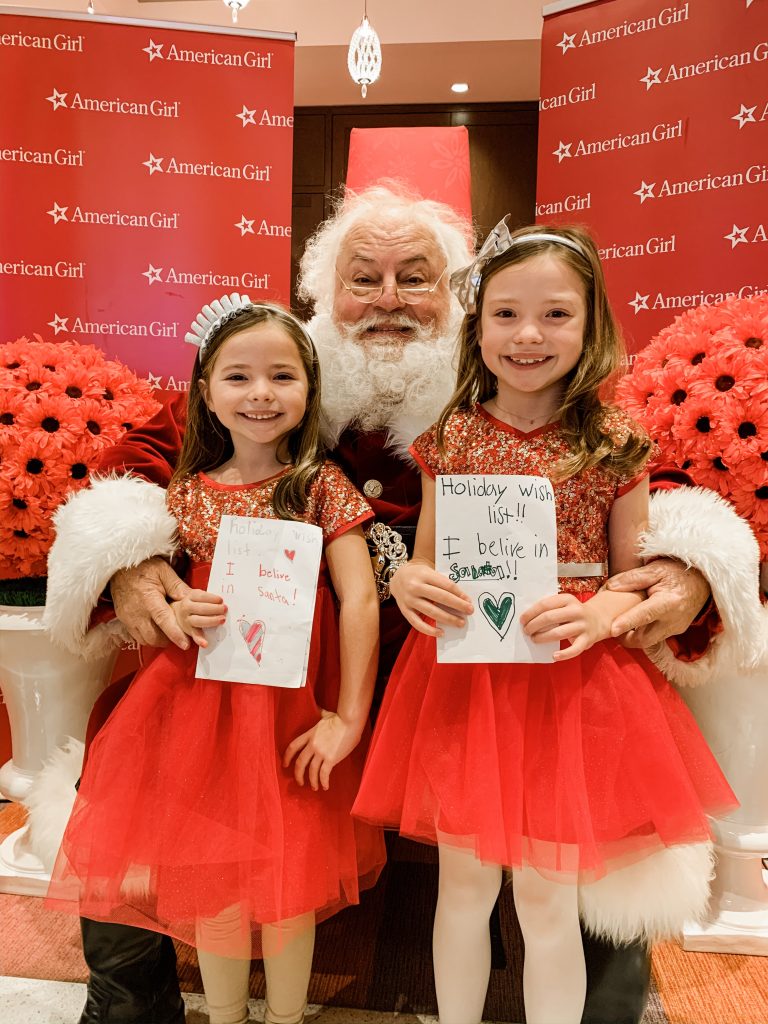 All Our Favorite Family Holiday Traditions by popular life and style blog, Hello Happiness: image of two girls standing with Santa and wearing American Girl Decked Out Holiday Dress for Girls.