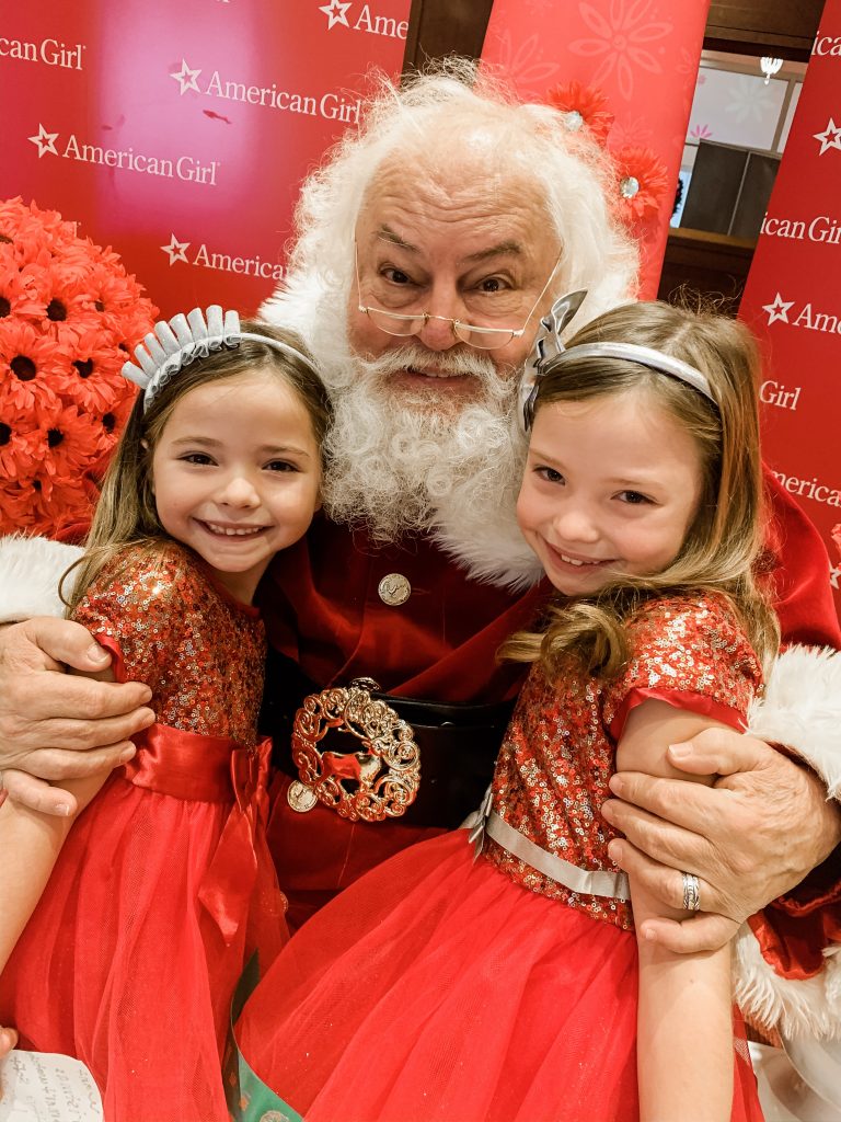 All Our Favorite Family Holiday Traditions by popular life and style blog, Hello Happiness: image of two girls standing with Santa and wearing American Girl Decked Out Holiday Dress for Girls. 