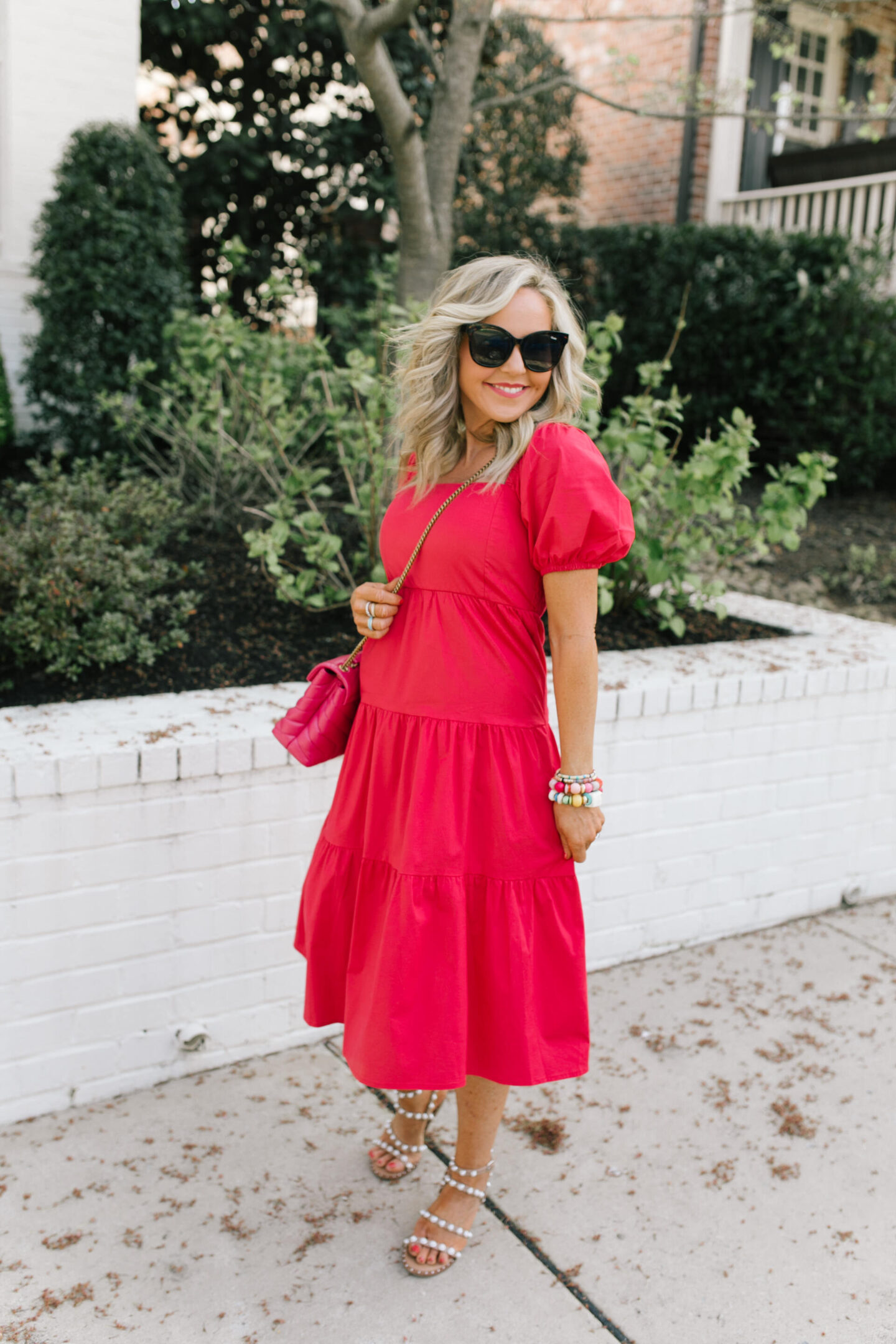All About Me by popular Nashville lifestyle blog, Hello Happiness: image of Natasha Stoneking wearing tiered pink midi dress, black frame oversized sunglasses, stack bracelets and clear studded strap sandals. 