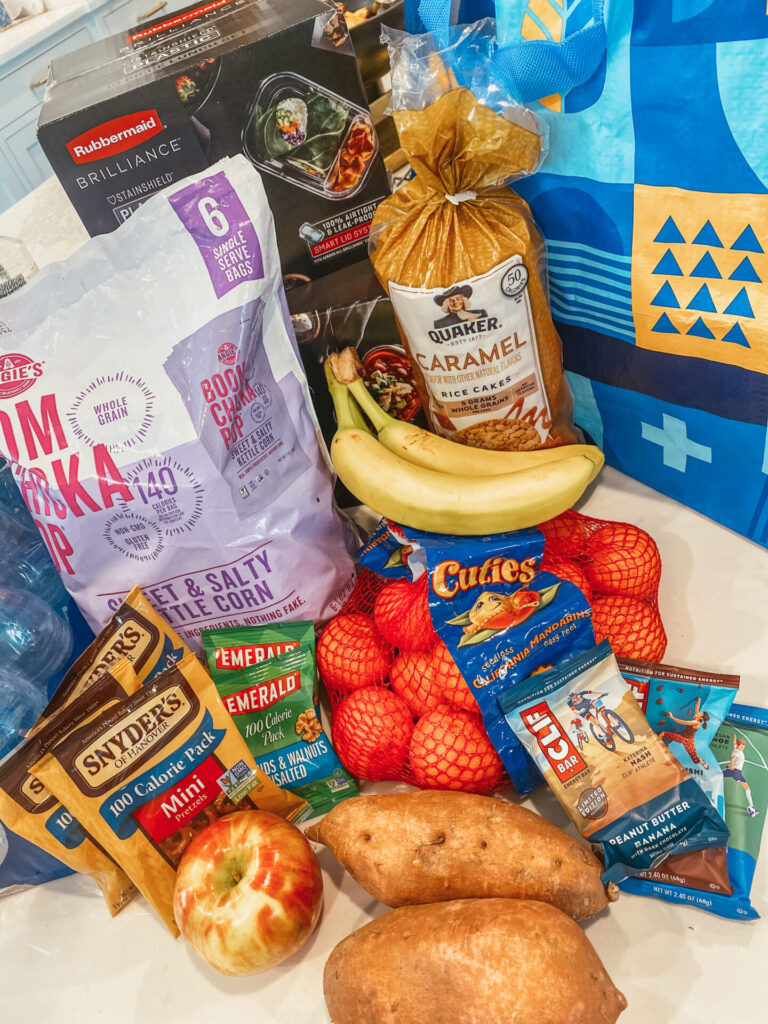 Walmart Membership by popular Nashville lifestyle blog, Hello Happiness: image of Boom Chicka Pop popcorn, bananas, Quaker popcorn cakes, sweet potatoes, cuties, cliff bars, Snyder's pretzels, apples and a reusable Walmart shopping bag. 